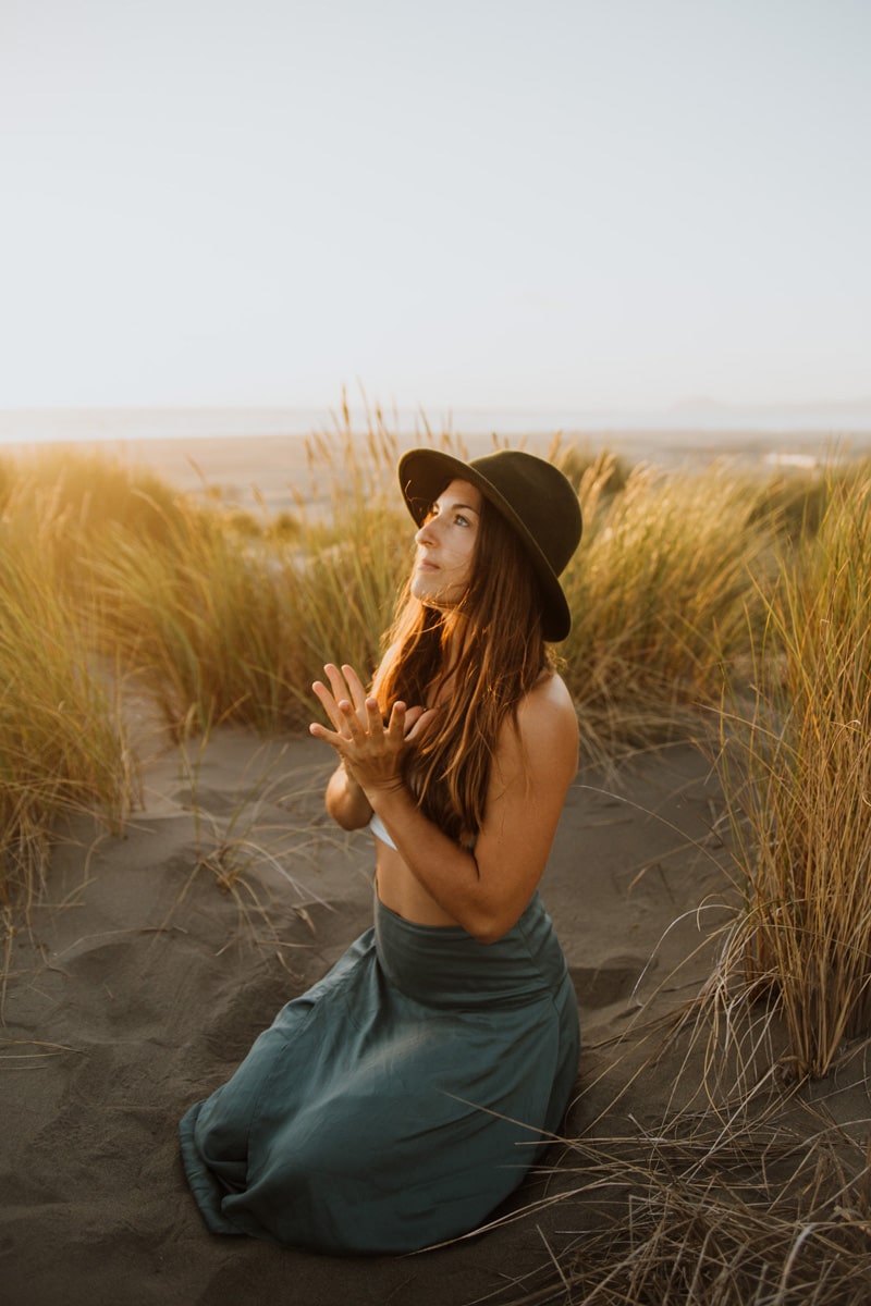 empowered online spiritual life coach sitting on the beach with hands open